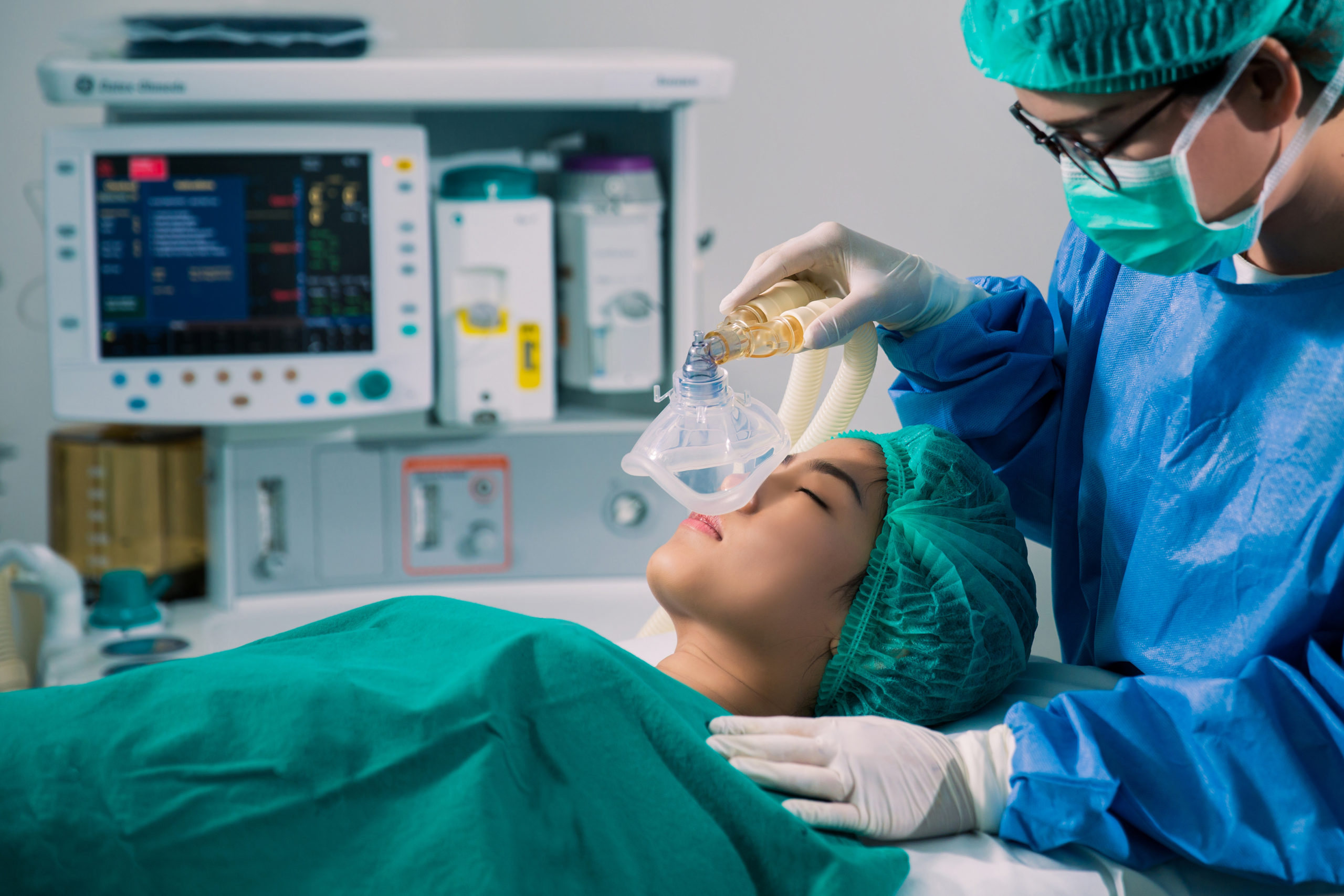 Patient in surgery/ Mask being put on for anethesia. Green scrubs on patient lying down with eyes closed.