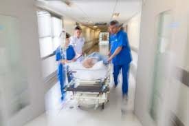 Blurred photo of doctors and nurses rushing a patient down a gurney in a hospital hallway.