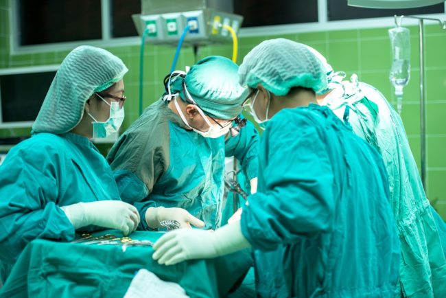 Photo of surgeons in blue-green scrubs huddled around operating table with surgical instruments next to them.